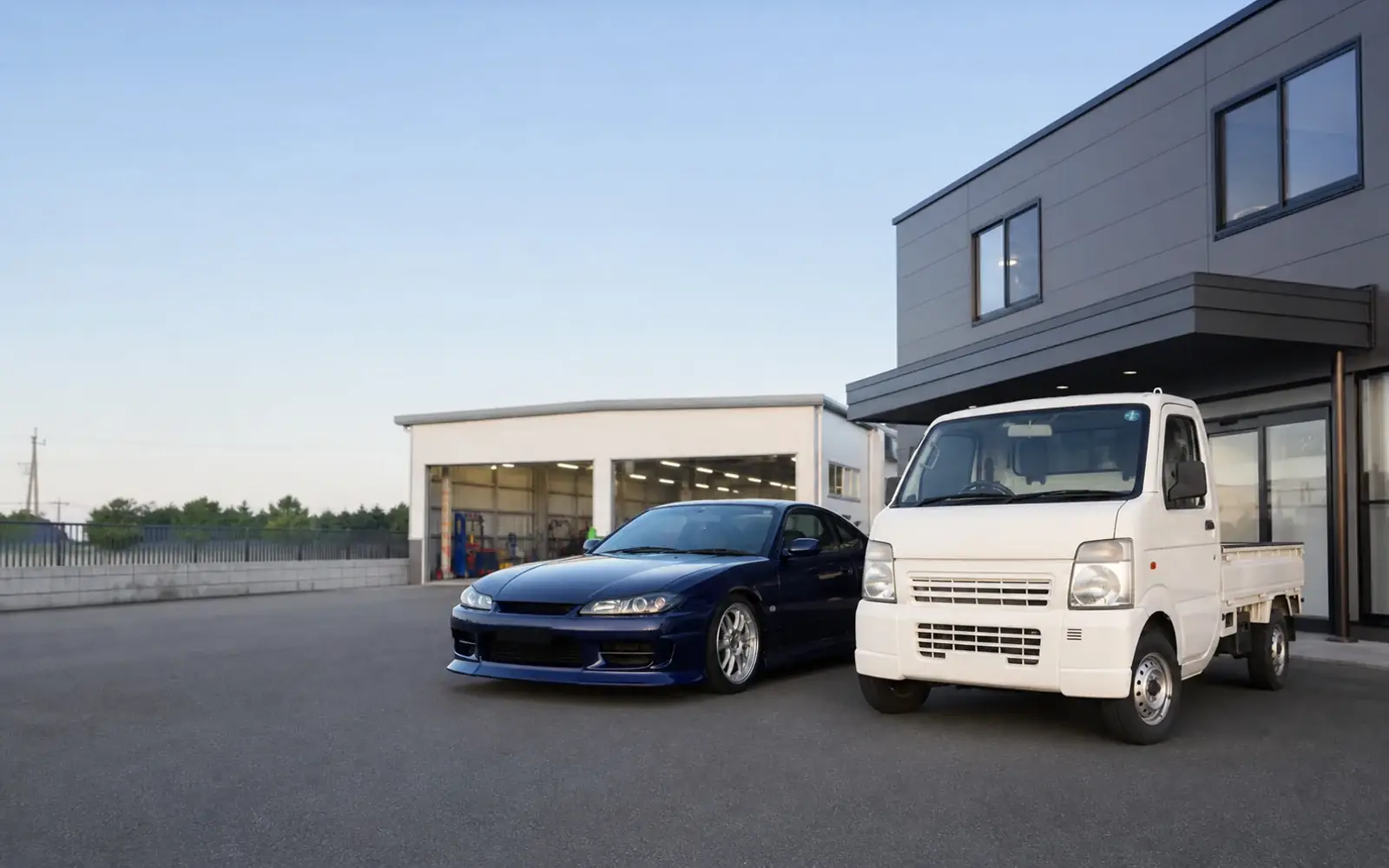 Japanese kei truck and sports coupe outside a vehicle-export workshop in Noda