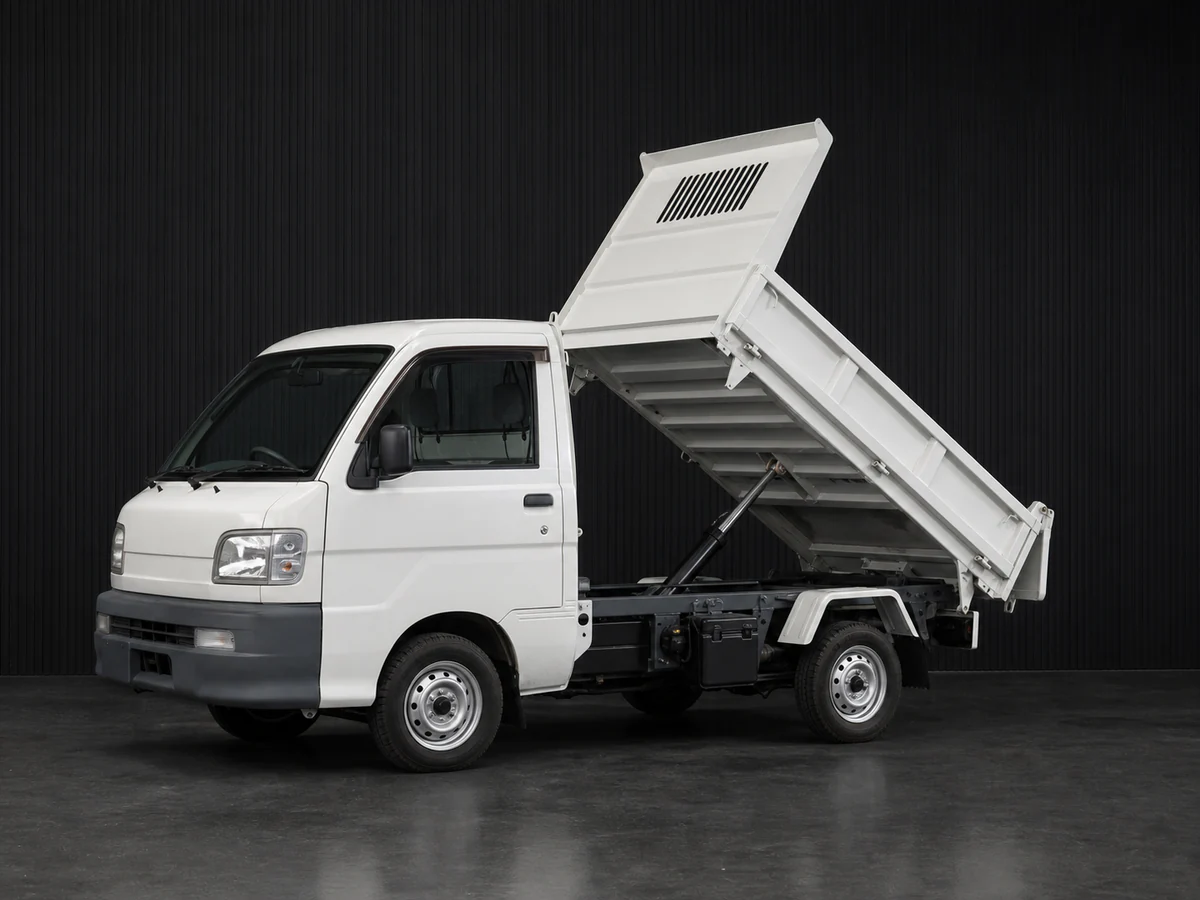 Daihatsu Hijet S211P-era dump kei truck with its bed raised in a dark grooved-wall studio