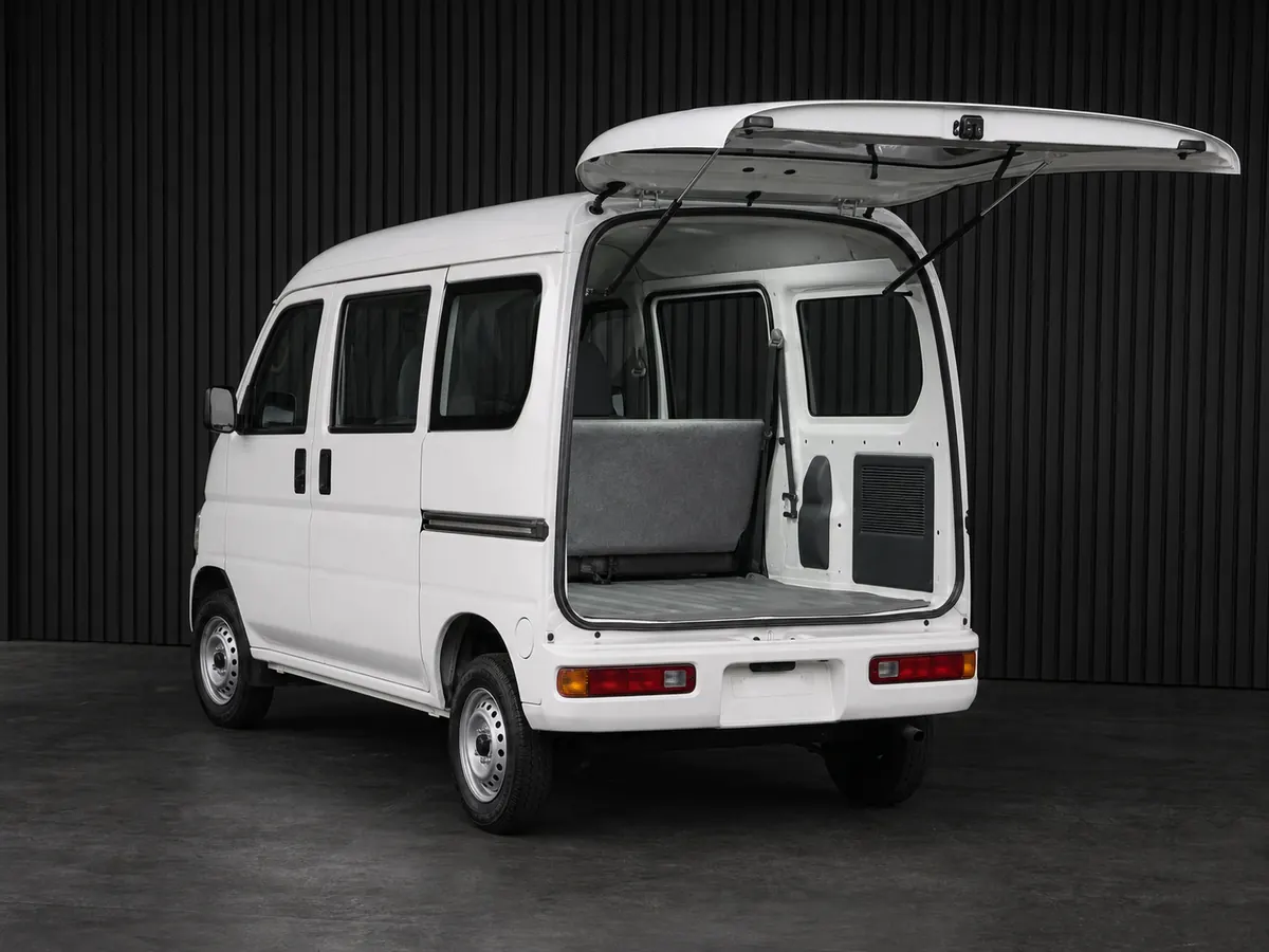 White Honda Acty-style cargo kei van with rear hatch open in a grooved-wall studio
