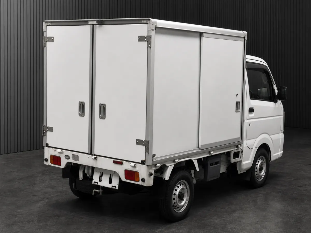 Rear three-quarter view of an older white kei truck with a smooth enclosed cargo box