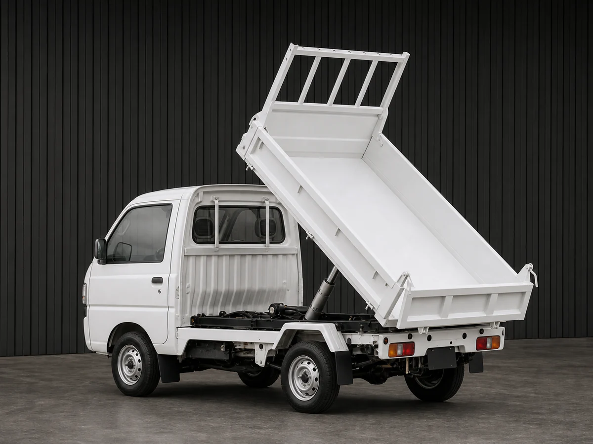 Subaru Sambar TT2 shallow dump kei truck with its bed raised in a dark grooved-wall studio