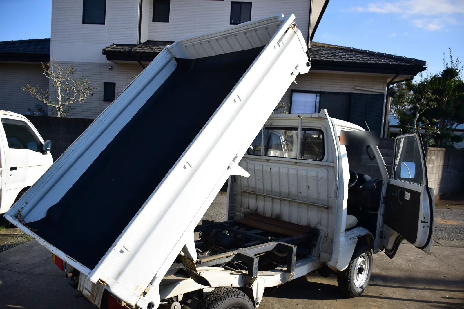 Suzuki Carry dump kei truck with the bed raised and a bed mat fitted